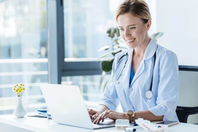 smiling-adult-female-doctor-in-white-coat-using-la